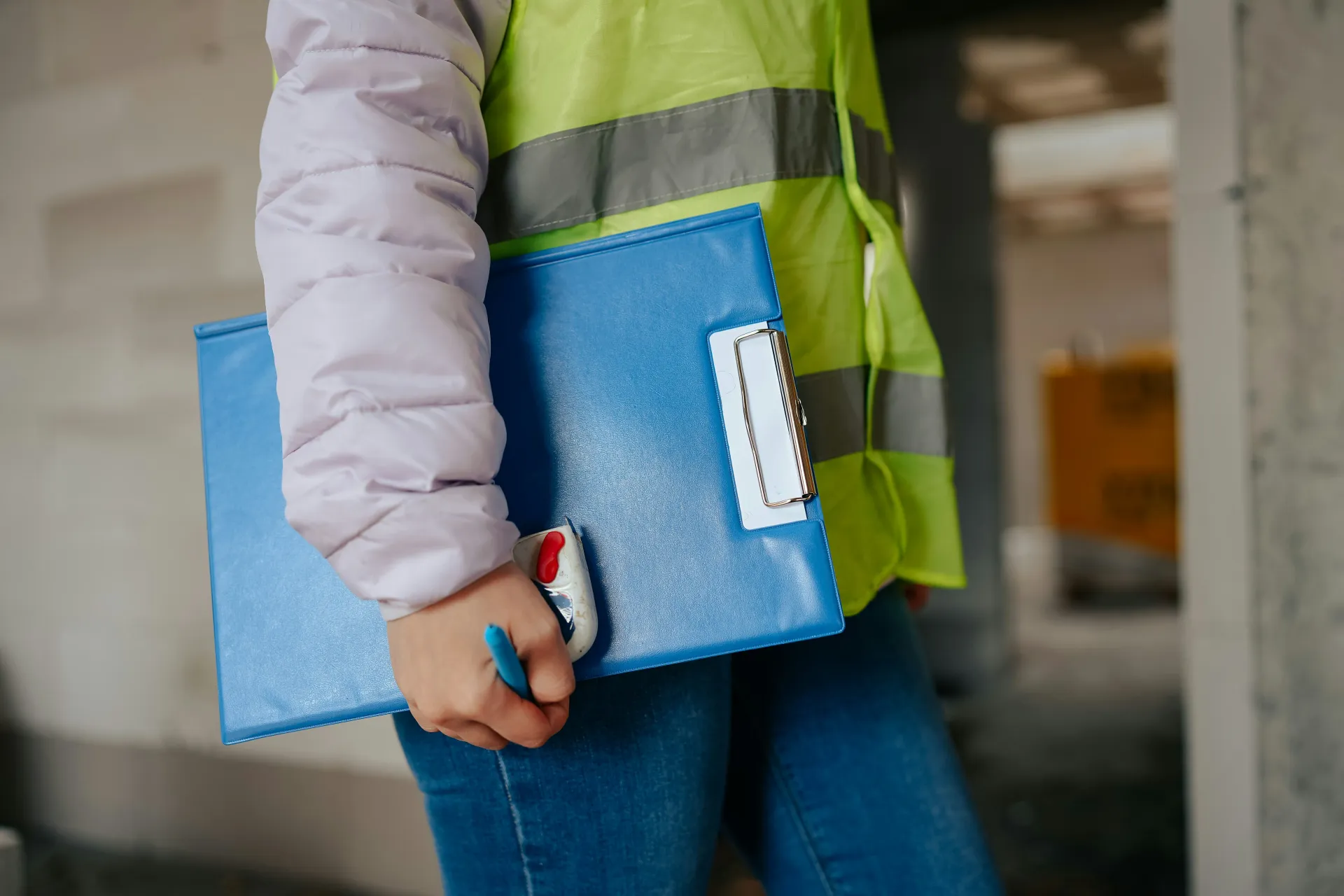 Close-up of an asbestos surveyor wearing a high-visibility vest and holding a blue clipboard and pen.