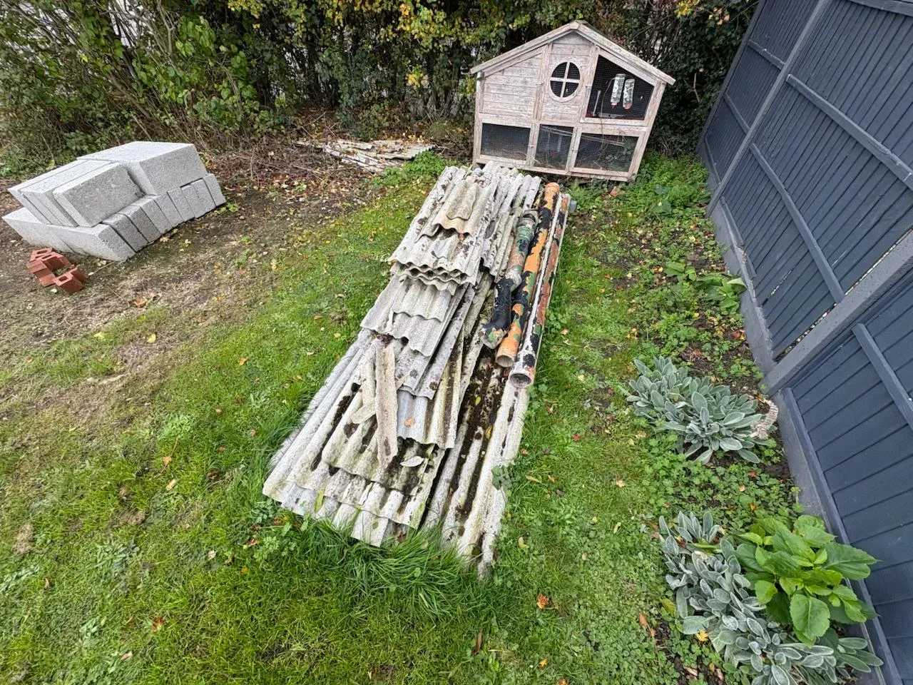 A pile of removed asbestos garage roof sheets on grass, ready for disposal